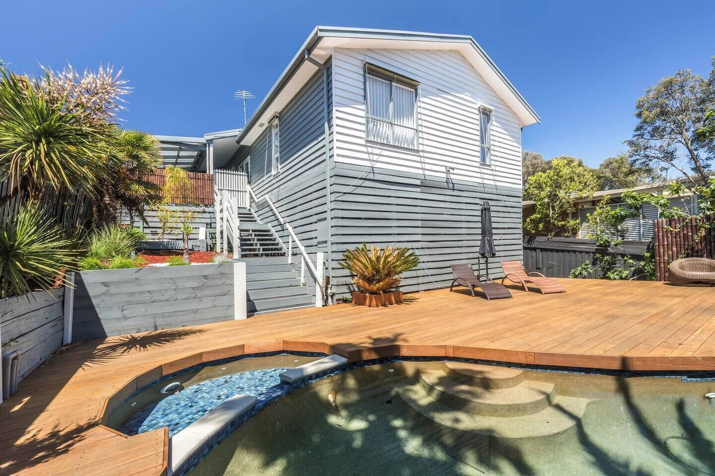 Une maison à deux étages dotée d’une terrasse, d’une petite piscine et d’un escalier menant à l’étage supérieur.