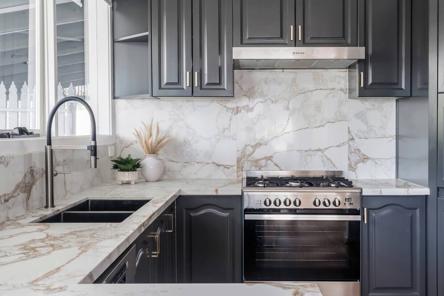 A kitchen with dark cabinets, a stainless steel range hood, and a marble backsplash.