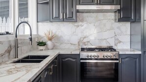 A kitchen with dark cabinets, a stainless steel range hood, and a marble backsplash. - Foreshore Haven Poolside Comfort near Rye Beach (Rye)