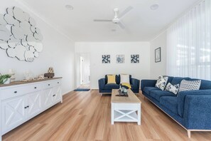 Ein modernes Wohnzimmer mit Holzboden, einem weißen Schrank, einer blauen Sofagarnitur und einem Deckenventilator.