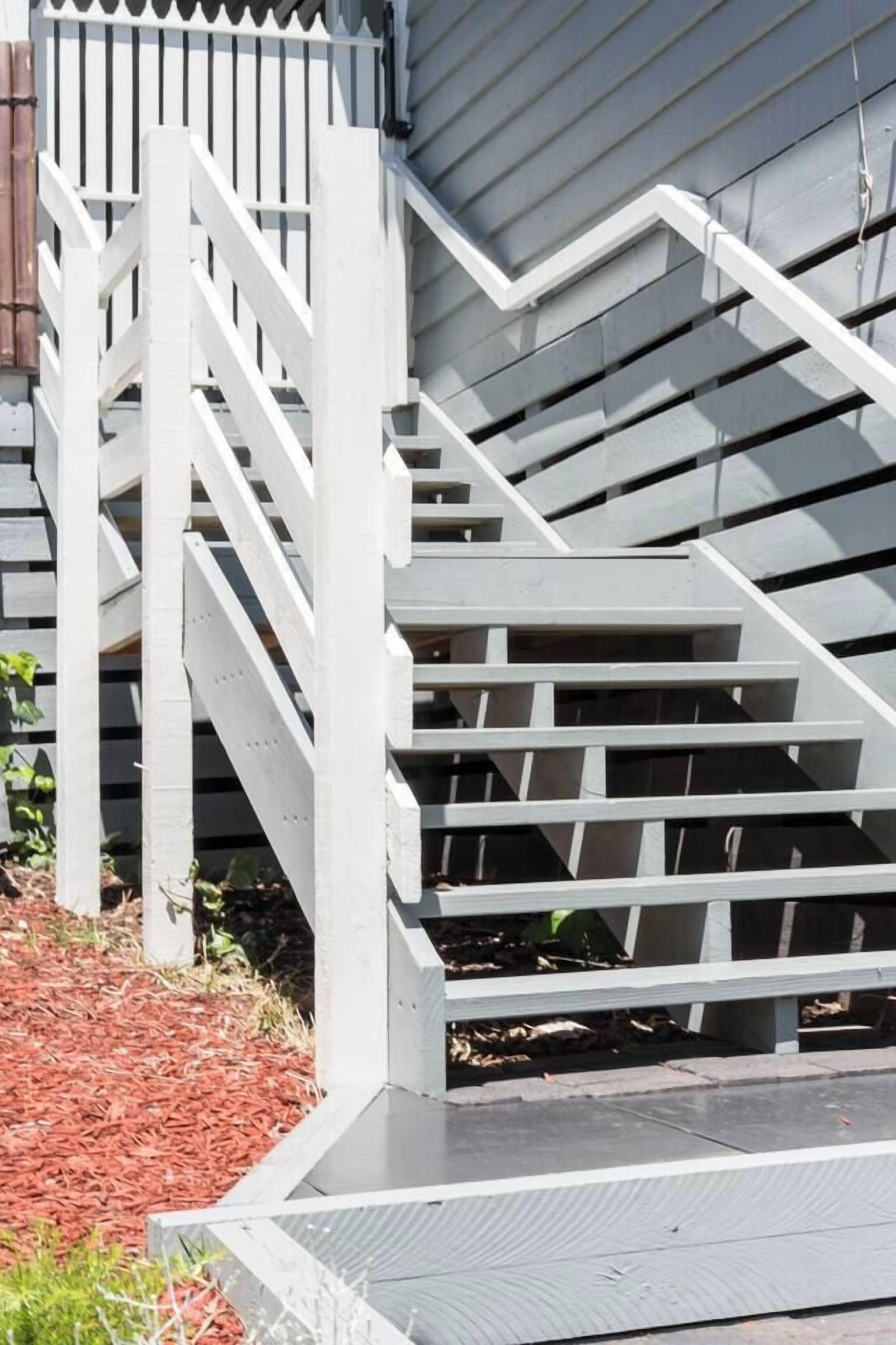A set of outdoor wooden stairs leading up to a building with a white picket fence.