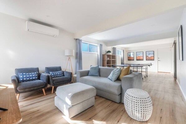 Una sala de estar moderna con un sofá gris, dos sillones, una mesa de centro y un pouf blanco.