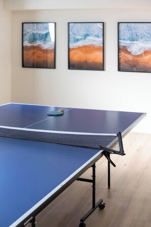 Ein Tischtennis-Tisch mit Netz in einem Raum mit Holzboden und drei gerahmten Kunstwerken an der Wand.