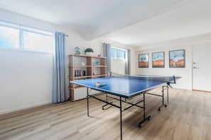 A room with a ping pong table, a bookshelf, and a door with artwork. - The Shack Your Ultimate Family Escape by the Sea (Rye)