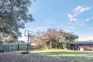 Basketballplatz mit Korb, umgeben von Bäumen und einer Werkstatt.