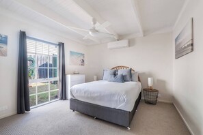 A bedroom with a bed, a ceiling fan, a window with curtains, and a wall-mounted air conditioner. - The Shack Your Ultimate Family Escape by the Sea (Rye)