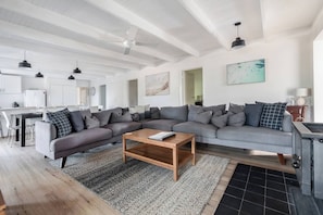 A modern living room with a grey sectional sofa, a wooden coffee table, and a kitchen area in the background. - The Shack Your Ultimate Family Escape by the Sea (Rye)