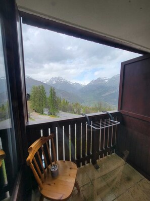 Un balcon avec une chaise en bois et un présentoir en métal, donnant sur un paysage montagneux.