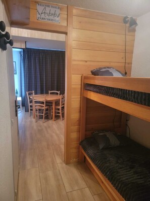 A room with a bunk bed, a wooden dining table with chairs, and a sign above the door. - Panoramic View of the Ecrins - Balcony at 1,700 - Sleeps 4–6 (Puy Saint Vincent)