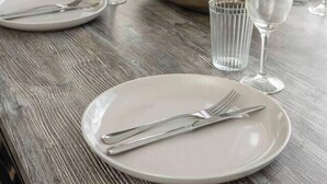 A dining table set with plates, cutlery, and glasses, with a plant and window in the background. - Seventh and Shore Spacious Poolside Group Getaway (Rosebud)
