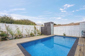 Uma piscina retangular com um deck de madeira, cercada por uma cerca branca, e um pequeno galpão ao fundo.