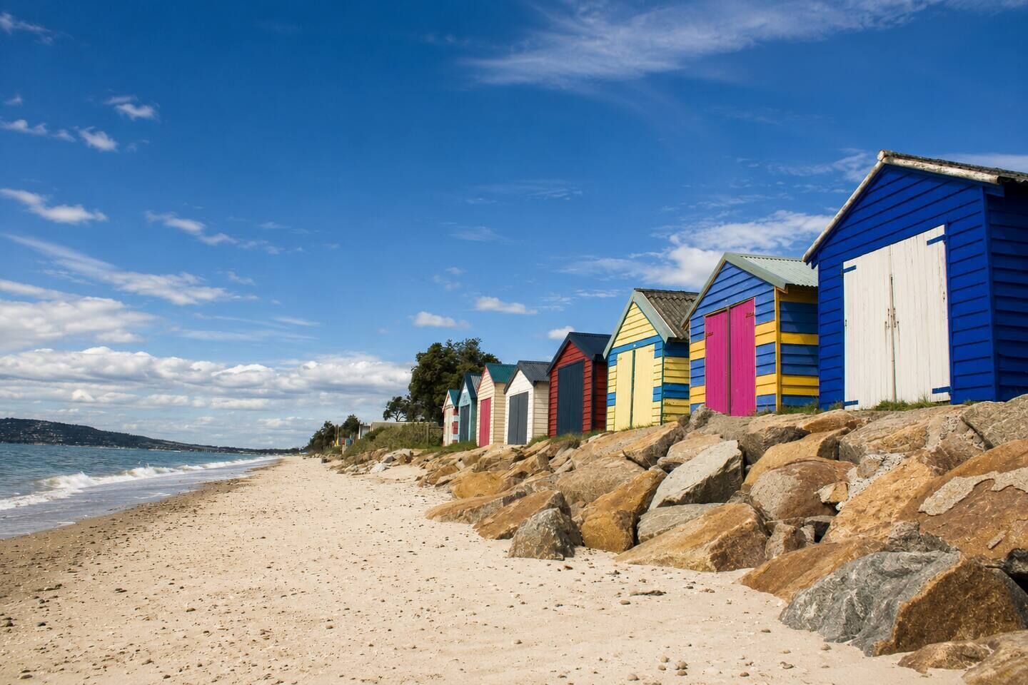 A beach with colorful beach huts and a rocky shoreline.