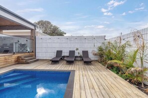 Ein Poolbereich mit Holzterrasse, drei Liegestühlen und einem weißen Zaun.