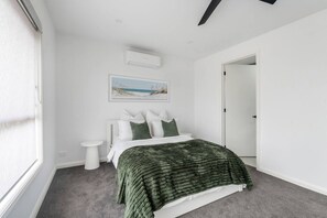 Quarto com cama, mesa de cabeceira, ar condicionado fixado na parede e um quadro emoldurado.