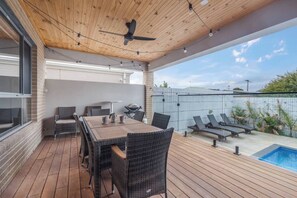 Eine Terrasse im Freien mit Holzboden, Tisch und Stühlen, Deckenventilator und Schwimmbad.
