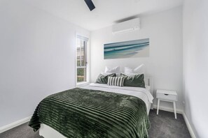 A bedroom with a bed, a nightstand, a window, and a painting on the wall. - Seventh and Shore Spacious Poolside Group Getaway (Rosebud)