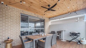 An outdoor patio with a brick wall, a ceiling fan, a table with chairs, and a grill. - Seventh and Shore Spacious Poolside Group Getaway (Rosebud)