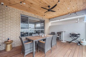 An outdoor patio with a brick wall, a ceiling fan, a table with chairs, and a grill. - Seventh and Shore Spacious Poolside Group Getaway (Rosebud)