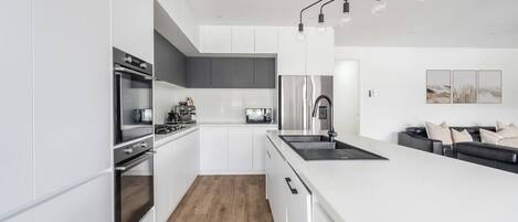 A modern kitchen with white cabinetry, a stainless steel refrigerator, and a black countertop.