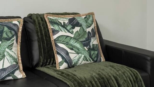 A black leather sofa with a green throw blanket and two pillows with a leaf pattern. - Seventh and Shore Spacious Poolside Group Getaway (Rosebud)