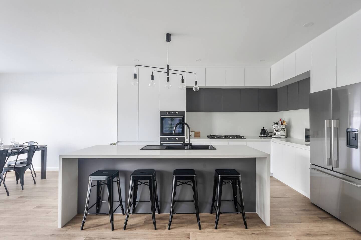 A modern kitchen with a central island, bar stools, a built-in oven, and a stainless steel refrigerator.