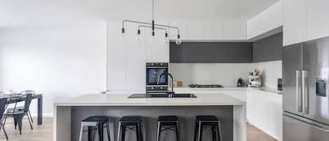 A modern kitchen with a central island, bar stools, a built-in oven, and a stainless steel refrigerator.