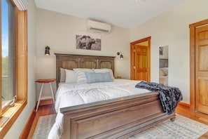 A bedroom with a wooden bed, a nightstand, a wall-mounted air conditioner, and a door leading to another room. - Large Luxury 6br Okemo Home | Hot Tub | Mtn View (Ludlow)
