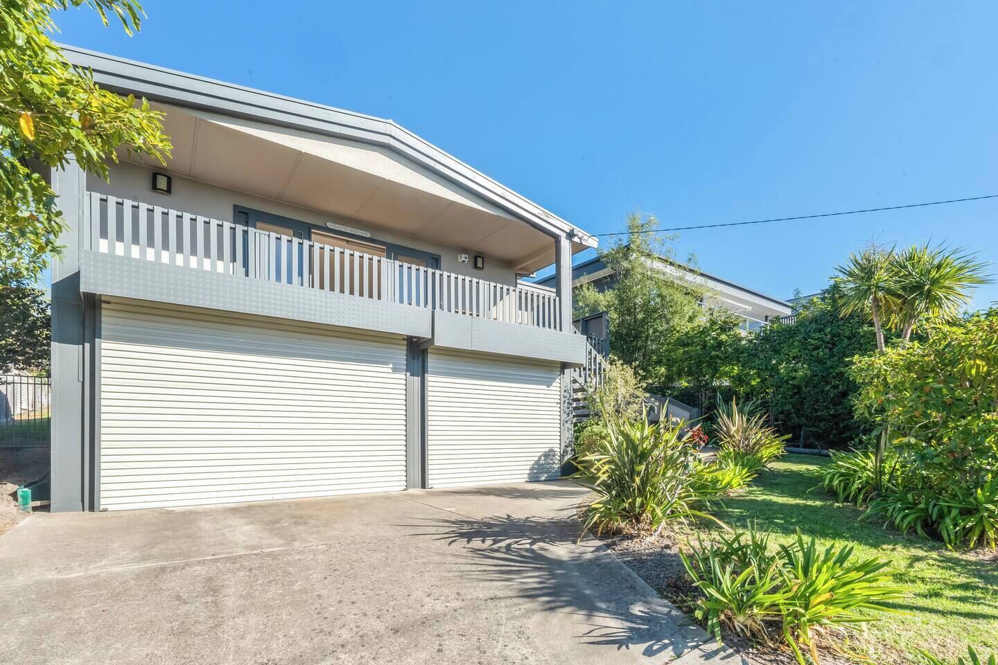 A two-story residential building with a flat roof, a balcony on the upper floor, and a garage with closed shutters.