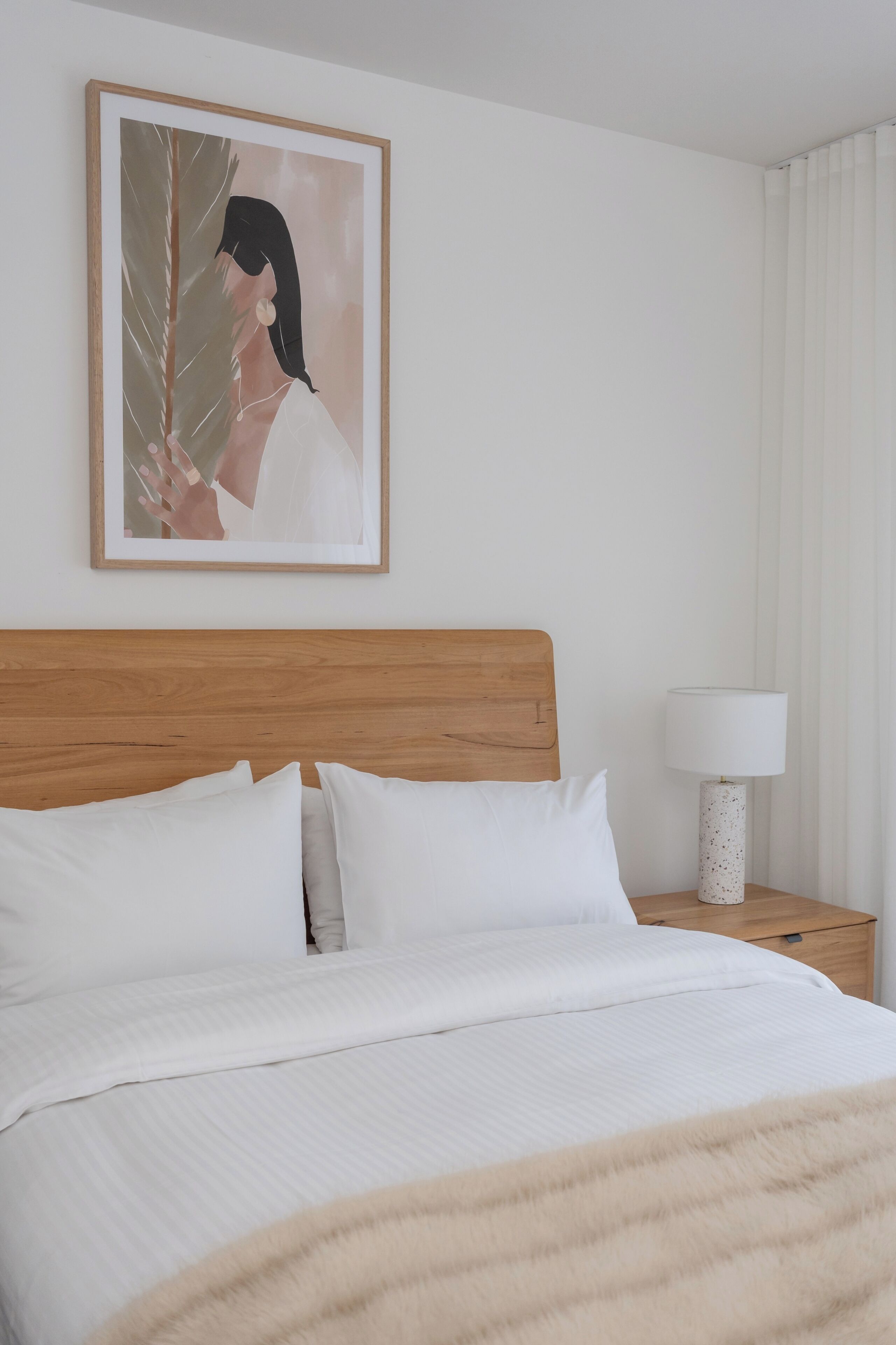 A neatly made bed with white linens, a wooden headboard, and a single bedside table with a lamp.