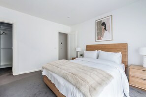 A bedroom with a bed, a nightstand, a bedside table, a lamp, a framed picture on the wall, and a closet with a hanger. - Reverie Poolside Haven near Beaches and Hot Springs (Rye)