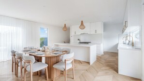 Una cocina moderna con armarios blancos, una isla central y un comedor con una mesa redonda y sillas.
