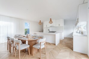 A modern kitchen with white cabinetry, a central island, and a dining area with a round table and chairs. - Reverie Poolside Haven near Beaches and Hot Springs (Rye)