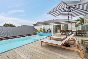 Une terrasse en bois avec une piscine, des chaises longues et un grand parasol à rayures.