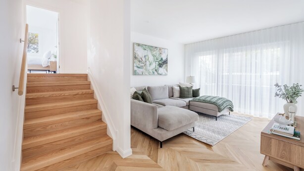 Una sala moderna con piso de madera en patrón chevron, un sofá seccional gris, un cuadro abstracto grande y una mesa de centro de madera.