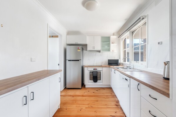 A modern kitchen with white cabinetry, a stainless steel refrigerator, a microwave, and a wooden countertop.