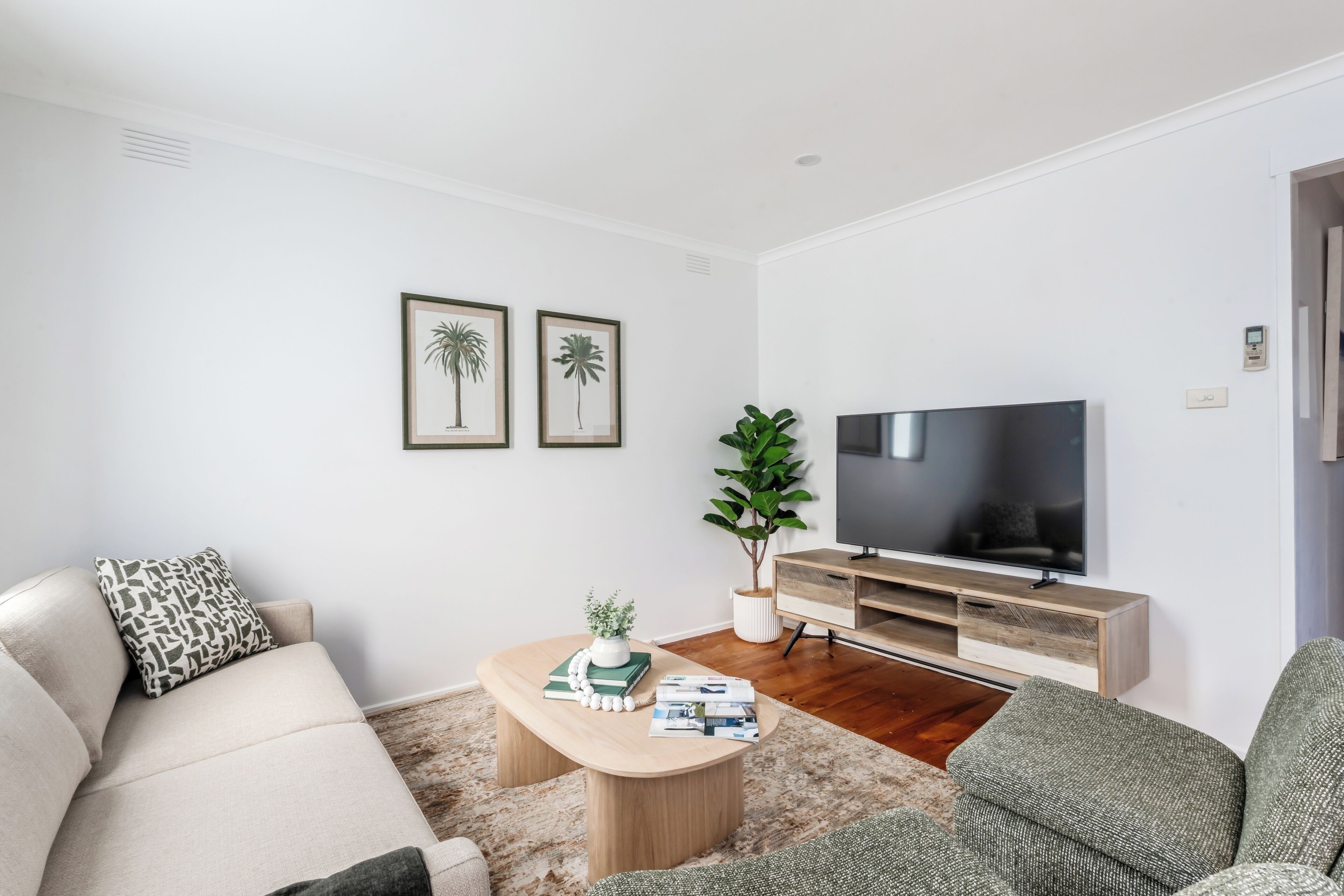 Un salon moderne avec un canapé, une table basse sur laquelle sont posés des livres et une plante, un téléviseur sur un meuble en bois, et deux tableaux encadrés accrochés au mur.
