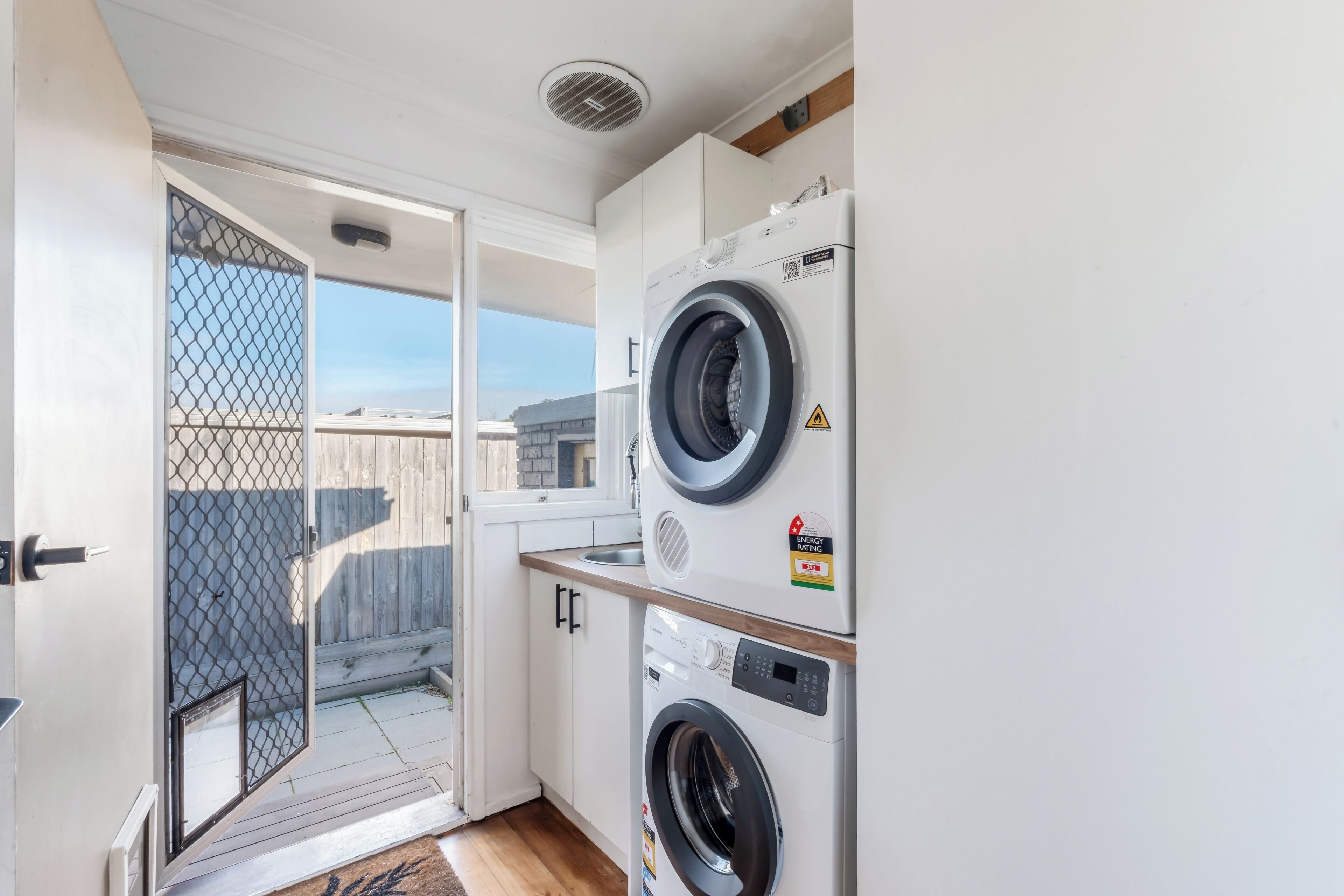 Una sala de bugaderia amb dues rentadores superposades, una finestra i una porta que dona a l'exterior.