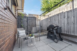 A patio area with wicker furniture, a grill, and a decorative fence.