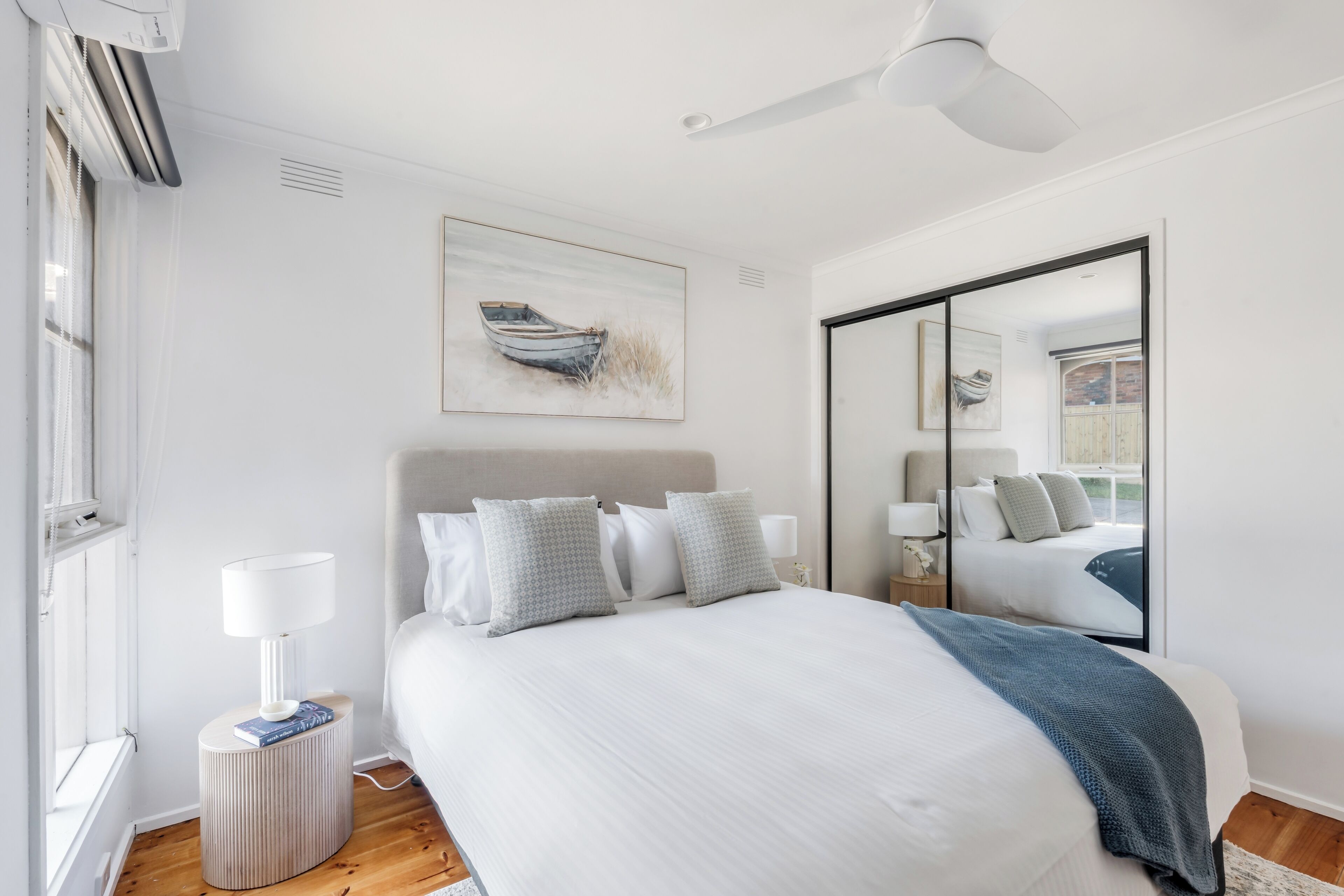 A modern bedroom with a bed, bedside lamps, a mirror, and a painting on the wall.