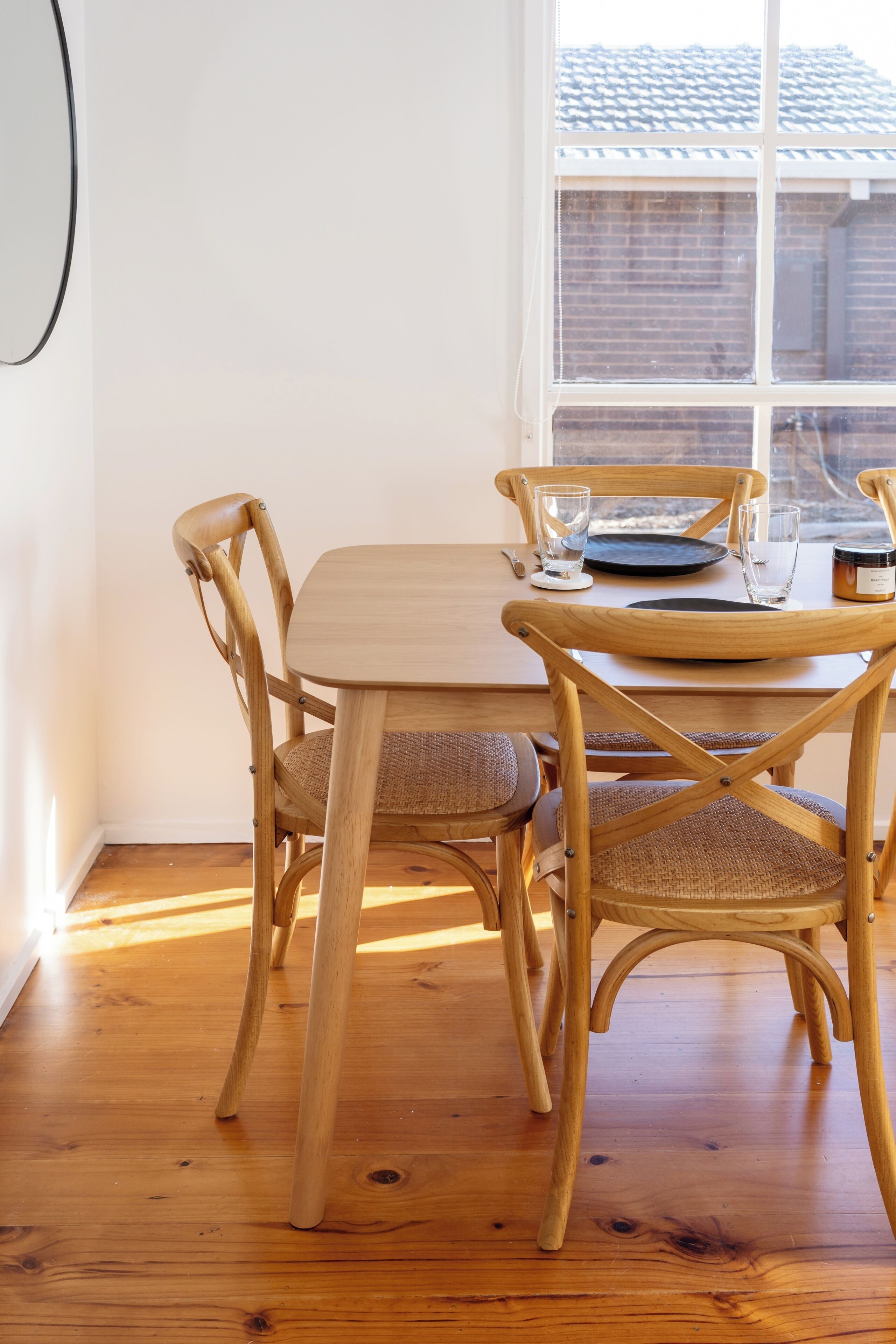 A wooden dining table with four chairs, a window with blinds, and a candle on the table.