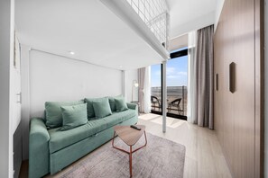 A modern living room with a green sofa, a small coffee table, and a view of the beach through large windows. - Stayshort - Minutes to Downtown - Sleek Meydan Apartment With Balcony - Sleeps 4 (Dubai)
