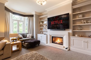 Una sala de estar con chimenea, televisor montado arriba y una estantería.