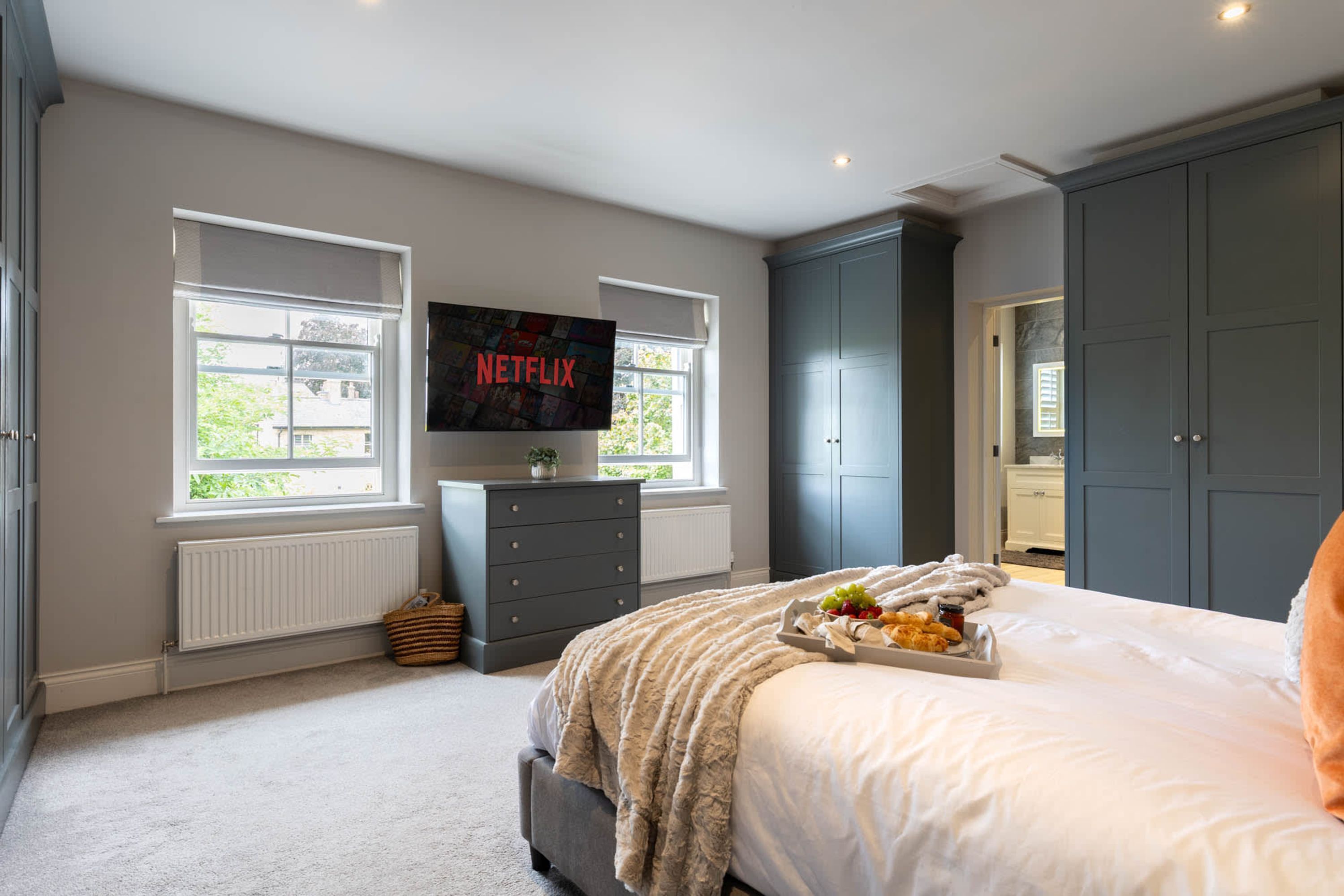 Une chambre à coucher avec un lit, une commode, un téléviseur affichant le logo « NETFLIX », et une fenêtre.