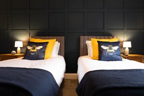Ein Hotelzimmer mit zwei Betten, jeweils mit Kopfteil, einem Nachttisch mit Lampe und einer Uhr.