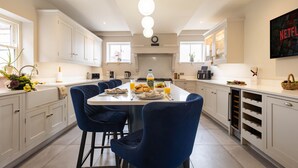 Una cocina moderna con armarios blancos, una isla central con sillas azules y un televisor de pantalla plana grande montado en la pared.