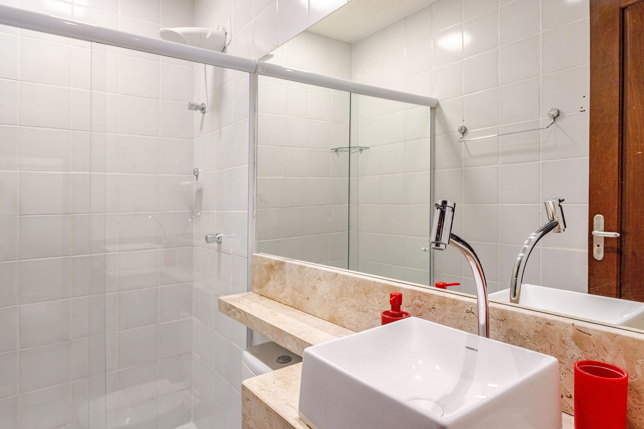 Un baño moderno con cabina de ducha de vidrio, un lavabo blanco y un espejo grande.