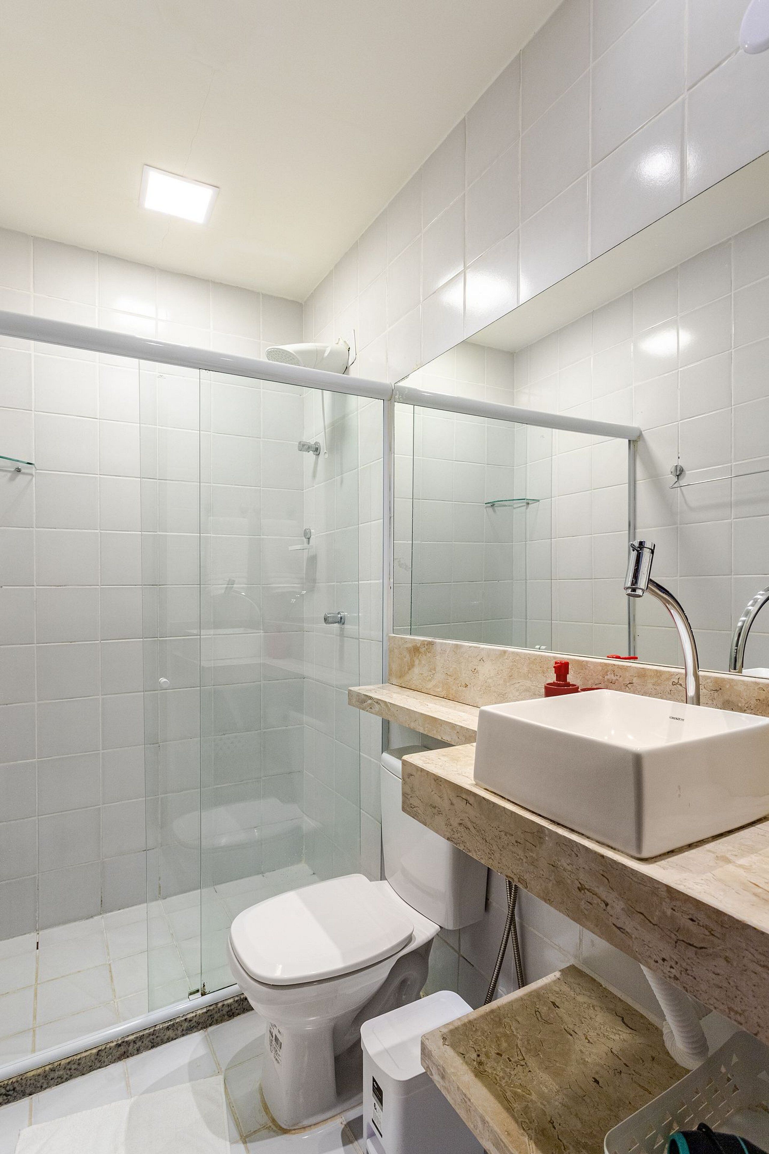Un baño moderno con ducha envuelta en vidrio, inodoro blanco y tocador con lavamanos y espejo.