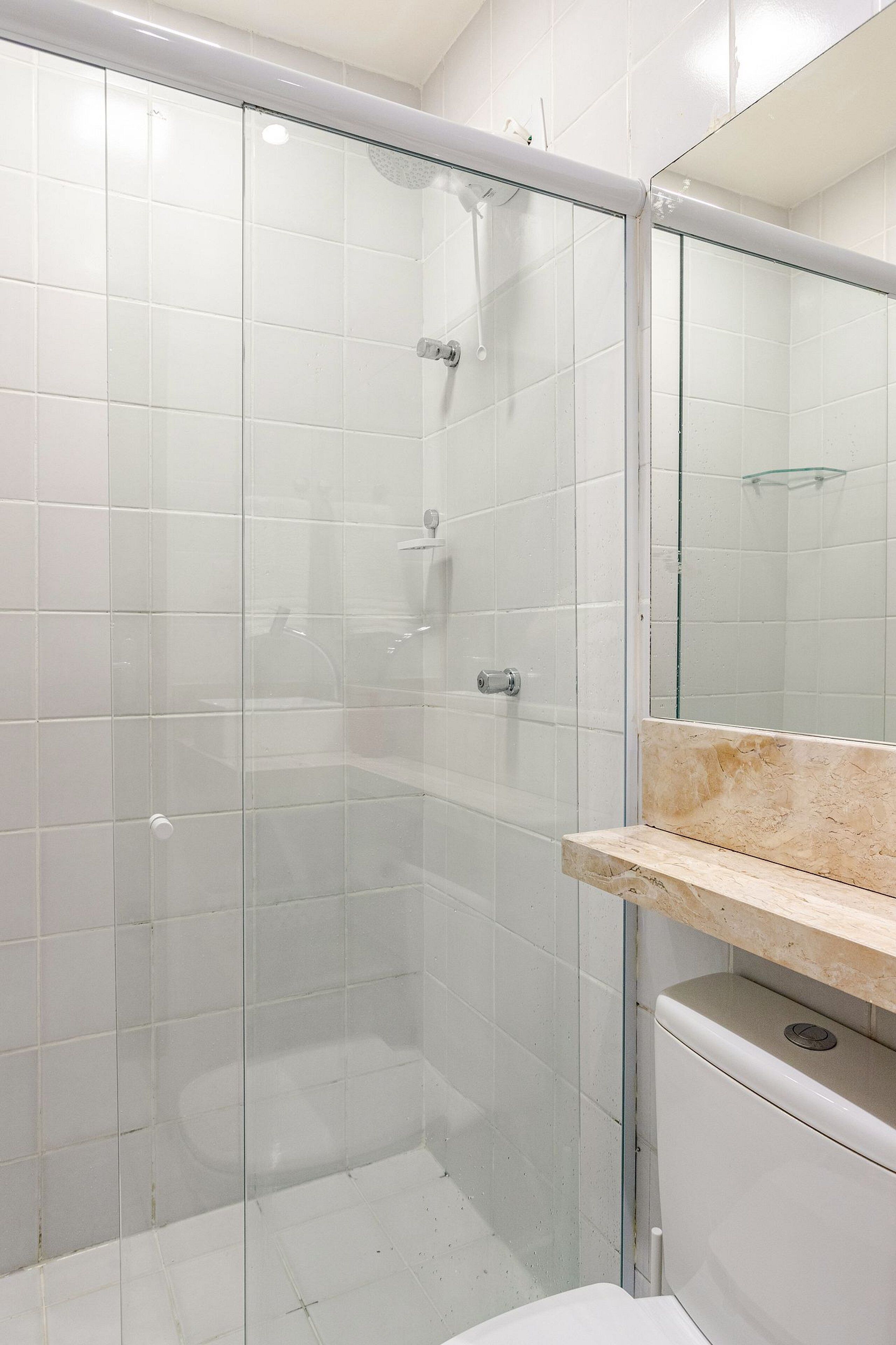 A modern bathroom with a glass-enclosed shower, white tiles, and a marble countertop.