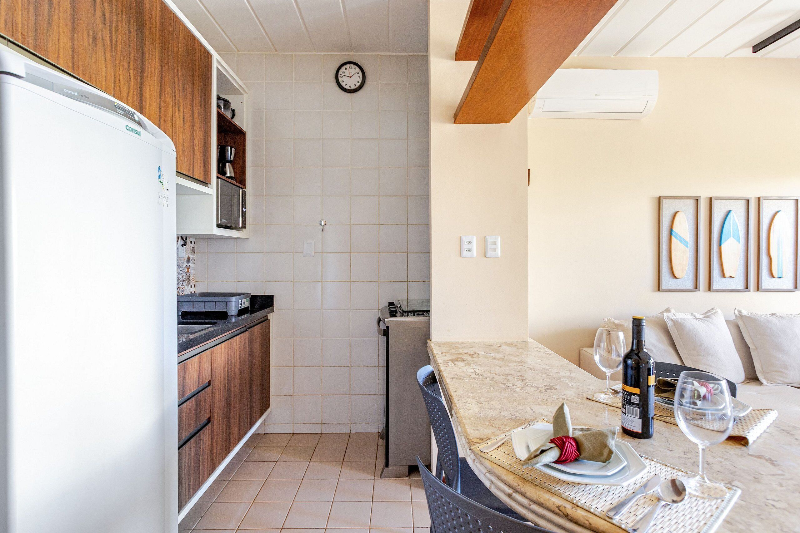 A compact kitchen with a refrigerator, microwave, and a clock on the wall.