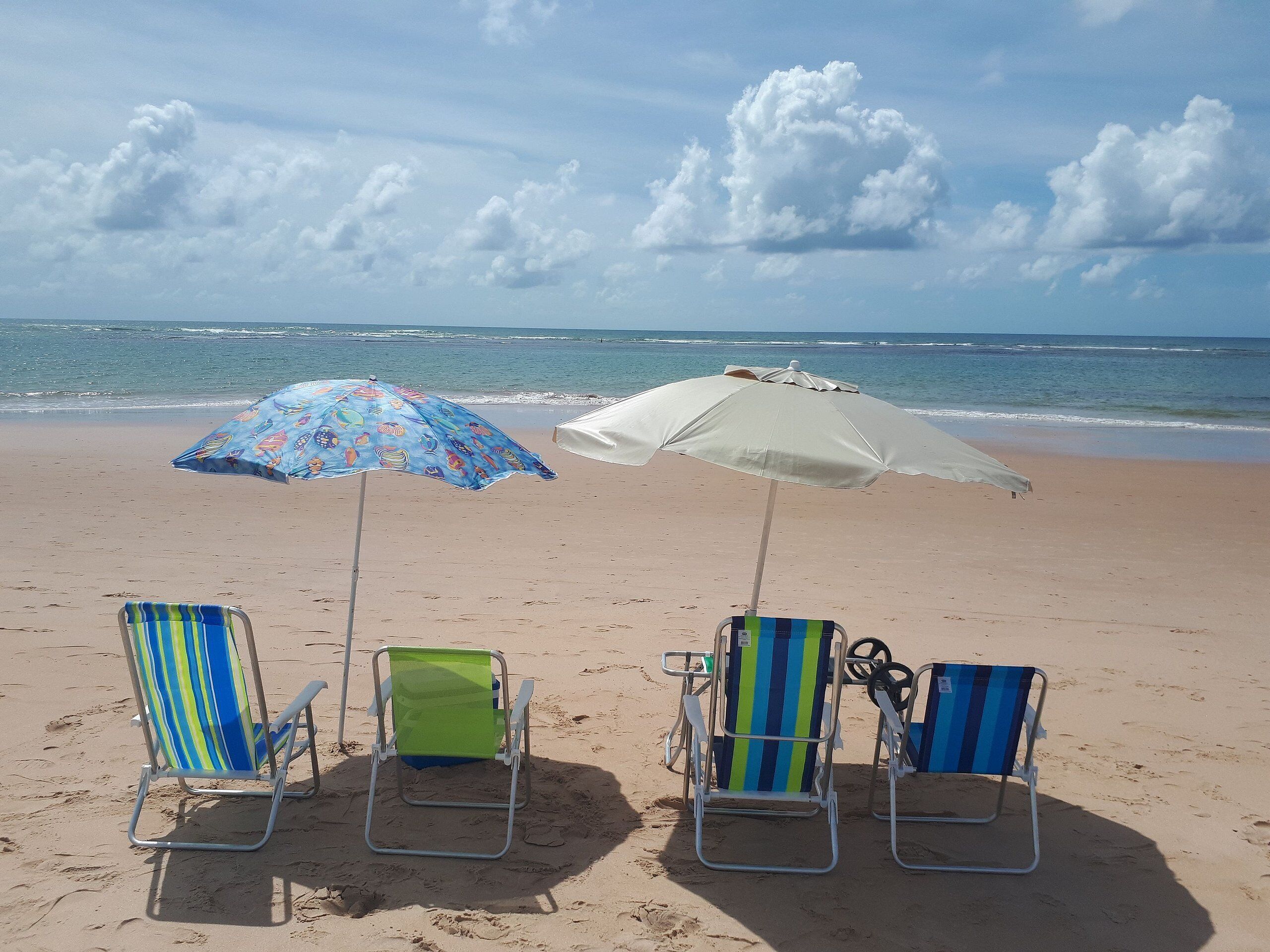 Una playa con tres sillas y dos sombrillas.